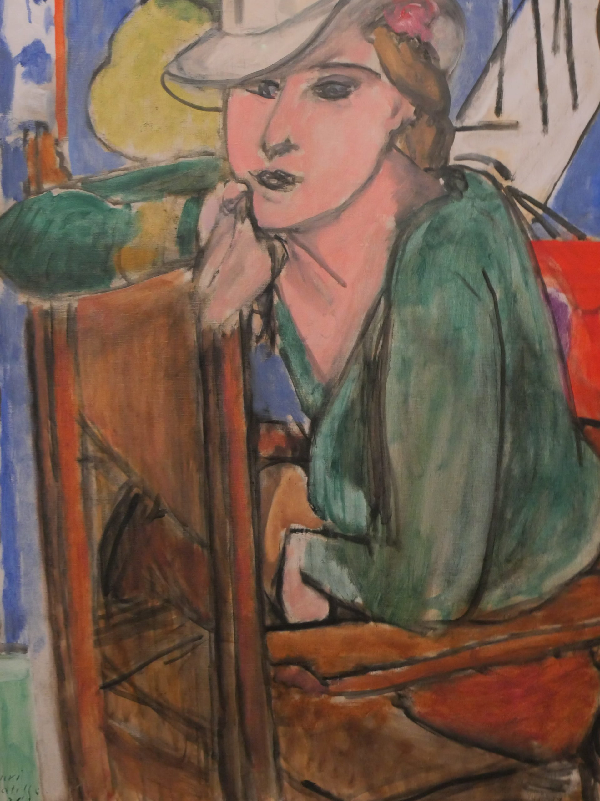 Femme accoudée à une chaise à l'envers portant une blouse verte et un chapeau